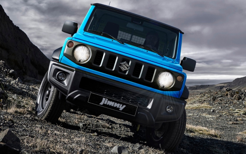 Suzuki Jimny azul, un vehículo todoterreno compacto, frente a un paisaje rocoso.